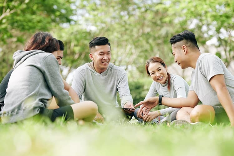 Group of young students sitting on a grass field having a discussion.